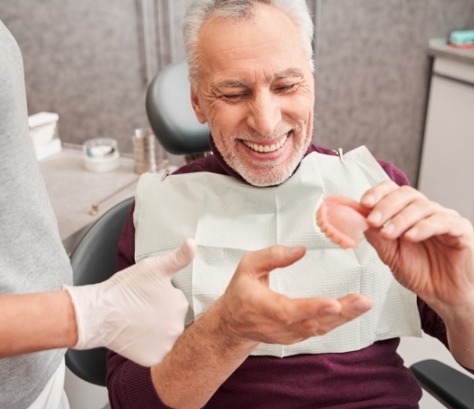 Senior dental patient smiling and holding dentures