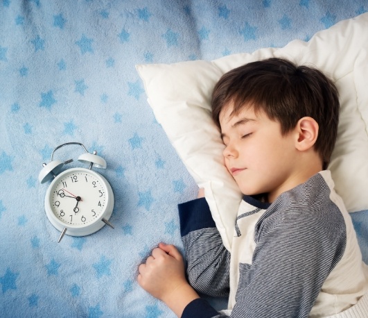 Boy sleeping in bed next to an alarm clock