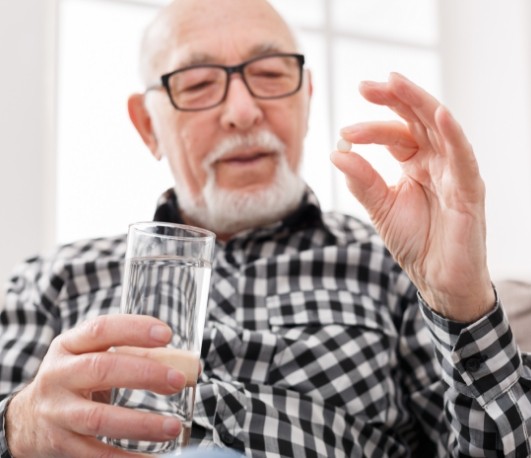 Senior man holding white pill and glass of water