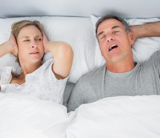 Woman in bed covering her ears next to snoring man