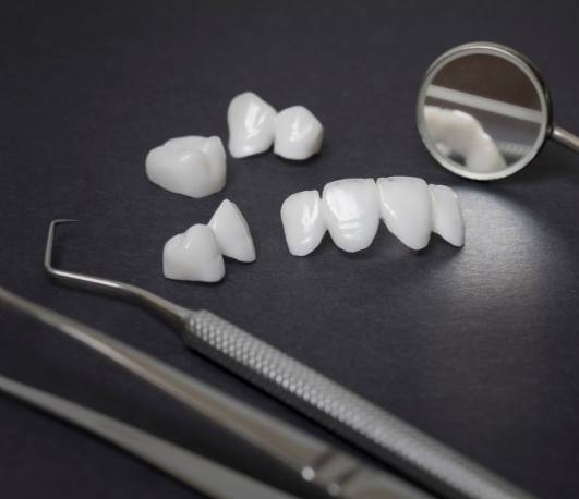 Several white dental crowns and veneers on desk next to dental mirrors