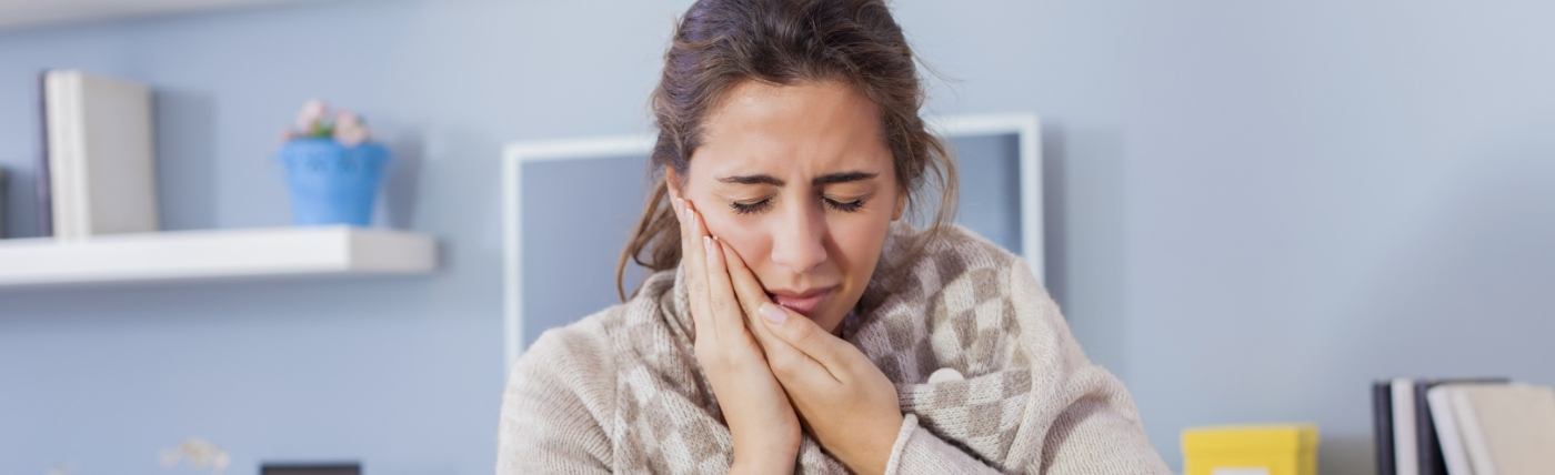 Woman holding her cheek in pain needing emergency dentist in Waco