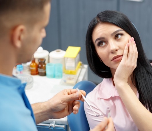 Woman holding her cheek while talking to emergency dentist