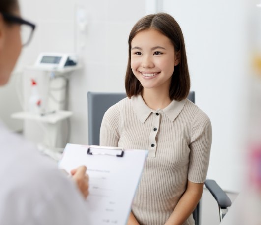 Woman smiling as dentist writes on clipboard