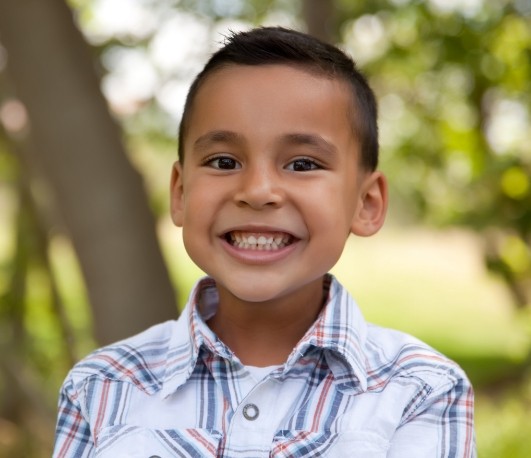 Boy grinning outside with tree in background