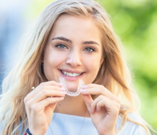 Smiling blonde woman holding an Invisalign tray