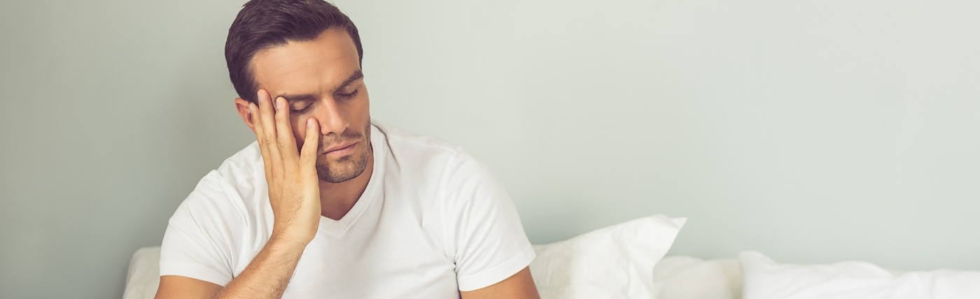 Exhausted man sitting up in bed before sleep apnea treatment in Waco