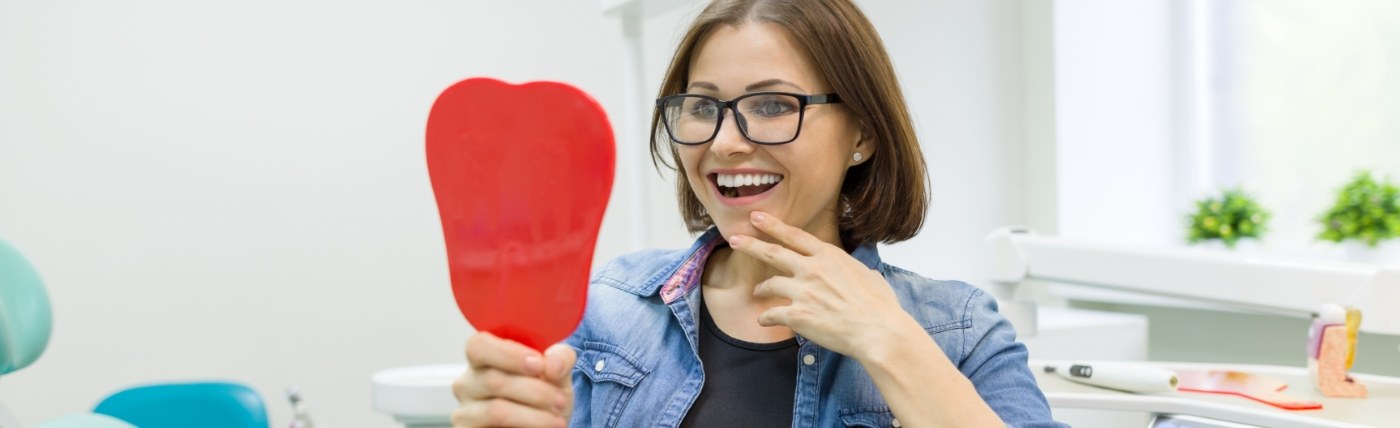 Dental patient admiring her smile in mirror after a smile makeover in Waco