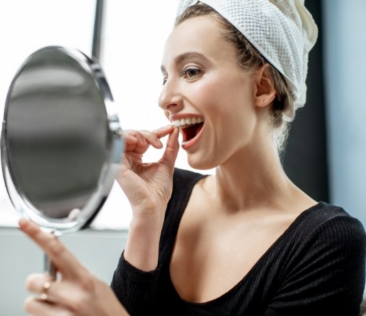 Woman looking in mirror and placing whitening tray over her teeth