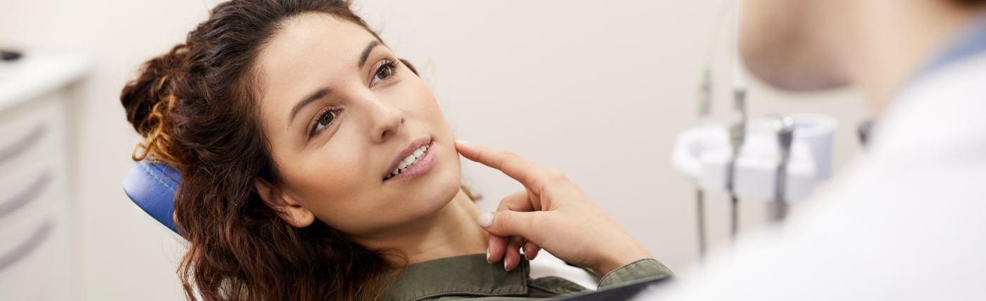 Woman in dental chair pointing to her mouth before getting tooth colored fillings in Waco