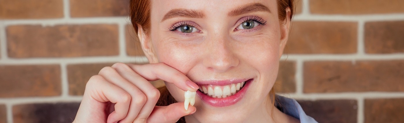 Smiling woman holding her tooth after a tooth extraction in Waco