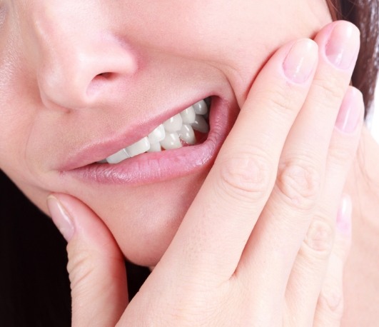 A woman holding her cheek in pain at the dentist office