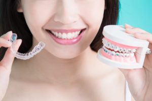 woman holding an Invisalign aligner and a model of teeth with braces 