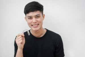 young man holding an aligner for Invisalign in Waco 