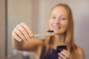 young woman holding toothbrush with charcoal toothpaste