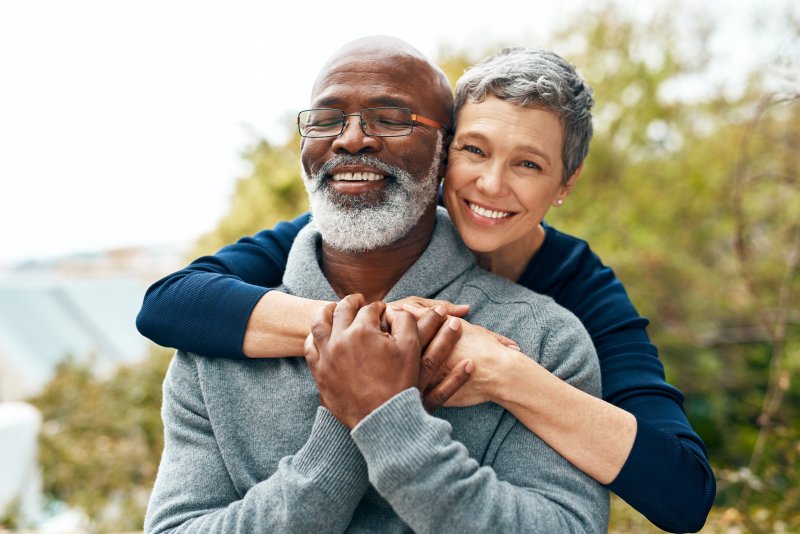 Older patient and partner smiling with dental implants